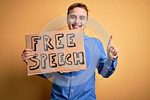 Young handsome redhead man asking for freedom holding banner with free speech message surprised with an idea or question pointing
