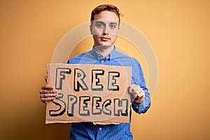 Young handsome redhead man asking for freedom holding banner with free speech message thinking attitude and sober expression