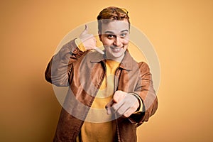 Young handsome redhead man wearing casual leather jacket over isolated yellow background smiling doing talking on the telephone