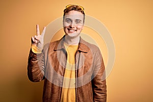 Young handsome redhead man wearing casual leather jacket over isolated yellow background smiling looking to the camera showing