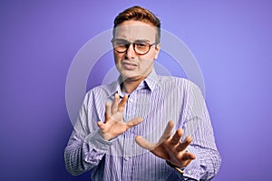 Young handsome redhead man wearing casual shirt and glasses over purple background disgusted expression, displeased and fearful