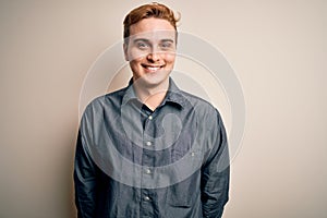 Young handsome redhead man wearing casual shirt standing over isolated white background with a happy and cool smile on face