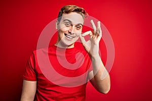 Young handsome redhead man wearing casual t-shirt over isolated red background smiling positive doing ok sign with hand and