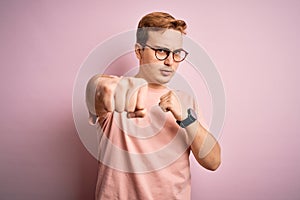 Young handsome redhead man wearing casual t-shirt standing over isolated pink background Punching fist to fight, aggressive and