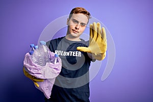 Young handsome redhead volunteer man doing volunteering holding bag with plastic bottles with open hand doing stop sign with