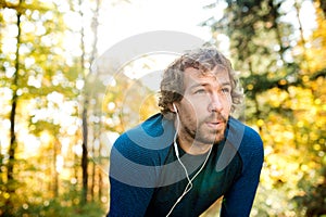 Young handsome runner with earphones outside in autumn nature