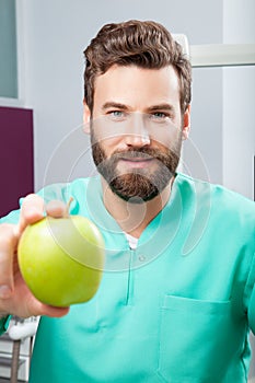 Young handsome serious male doctor with beard holding green apple