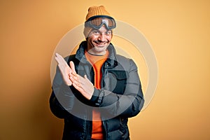 Young handsome skier man skiing wearing snow sportswear using ski goggles clapping and applauding happy and joyful, smiling proud