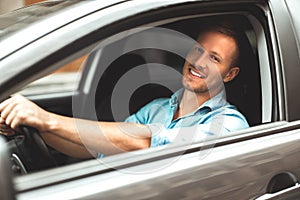 Young handsome smiling man driving car close up