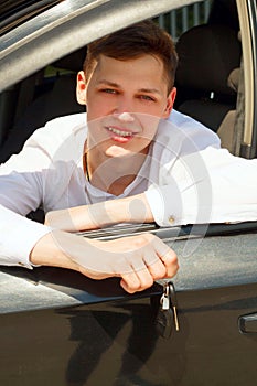 Young handsome smiling man sitting in his car at daylight holding keys in hands