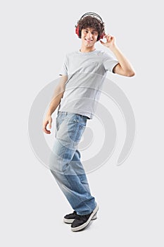 Young handsome smiling man wearing headphones to listen to music and dancing while looking into the camera, full body isolated photo
