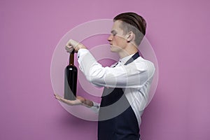 Young handsome sommelier opens a bottle of wine on a colored background, the guy the waiter holds red wine