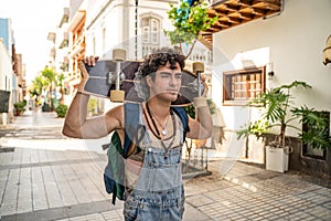 Young handsome spanish skater man holding waveboard and walking in the city. Happy fashionable  guy with skateboard. Hobby.