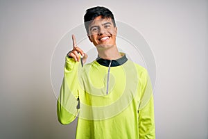 Young handsome sportsman doing sport wearing sportswear over isolated white background showing and pointing up with finger number