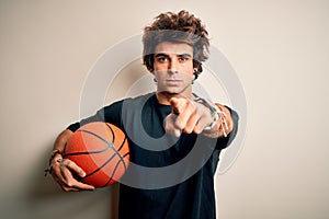 Young handsome sportsman holding basketball ball standing over isolated white background pointing with finger to the camera and to