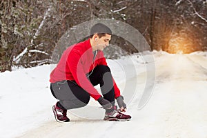 Young and handsome sportsman in red sweater ties shoelaces of his sneakers. Outdoor activity.