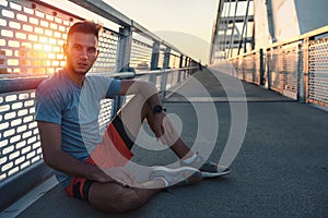 Young handsome sporty jogger taking break from exercising outdoors in the sunset