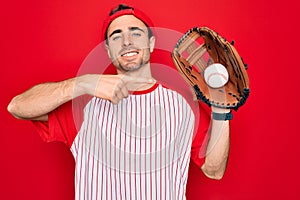 Young handsome sporty man with blue eyes playing baseball using glove and ball very happy pointing with hand and finger