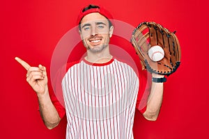 Young handsome sporty man with blue eyes playing baseball using glove and ball very happy pointing with hand and finger to the