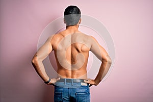 Young handsome strong man with beard shirtless standing over isolated pink background standing backwards looking away with arms on