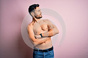 Young handsome strong man with beard shirtless standing over isolated pink background looking to the side with arms crossed