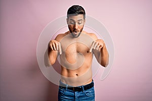 Young handsome strong man with beard shirtless standing over isolated pink background Pointing down with fingers showing