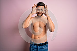 Young handsome strong man with beard shirtless standing over isolated pink background Trying to open eyes with fingers, sleepy and