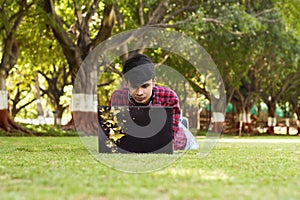 Young handsome student laying on grass and using laptop