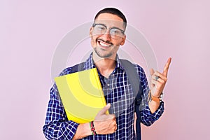 Young handsome student man holding a book over isolated background very happy pointing with hand and finger to the side