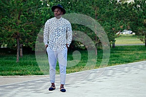 A young and handsome stylish model afro- american man in a stylish suit and a black hat in a summer park . latino