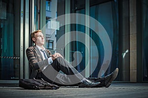 Young handsome successful stylish businessman sitting near modern office