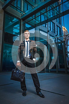 Young handsome successful stylish businessman standing near modern office