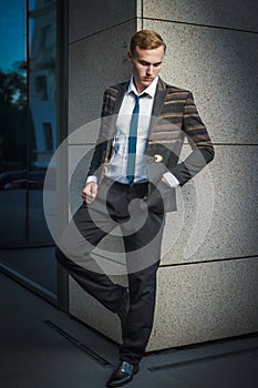 Young handsome successful stylish businessman standing near modern office