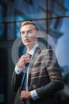 Young handsome successful stylish businessman standing near modern office