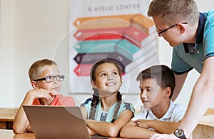 Young handsome teacher with group of clever children working with laptop during a lesson