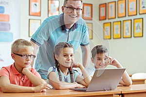 Young handsome teacher with group of clever children working with laptop during a lesson