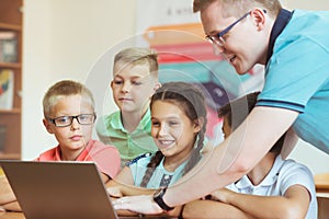 Young handsome teacher with group of clever children working with laptop during a lesson