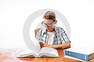 Young handsome teen guy reading book sitting at table, schoolboy or student doing homework, in Studio