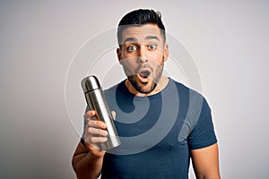 Young handsome tourist man drinking thermo with water over isolated white background scared in shock with a surprise face, afraid