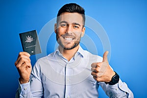 Young handsome tourist man holding australia australian passport id over blue background happy with big smile doing ok sign, thumb