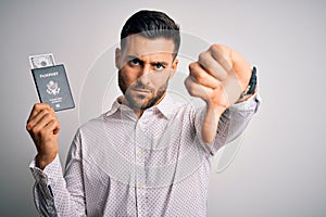 Young handsome tourist man holding united states passport id with dollars with angry face, negative sign showing dislike with