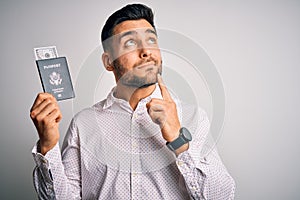 Young handsome tourist man holding united states passport id with dollars serious face thinking about question, very confused idea