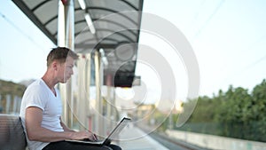 Young Handsome Tourist Man Sitting And Using Laptop While Waiting For The Train