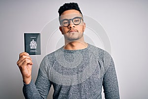 Young handsome tourist man on vacation wearing glasses holding Canada Canadian passport with a confident expression on smart face