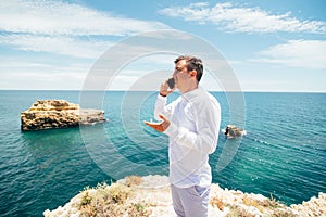 Young handsome traveler man in white t-shirt speak on the phone on the ocean background