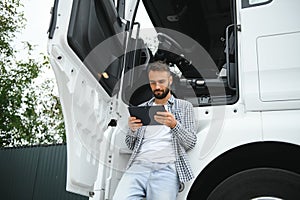 Young handsome truck driver is standing with a tablet near the truck