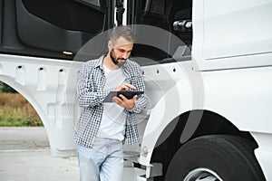 Young handsome truck driver is standing with a tablet near the truck