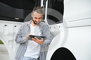 Young handsome truck driver is standing with a tablet near the truck