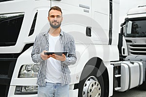 Young handsome truck driver is standing with a tablet near the truck