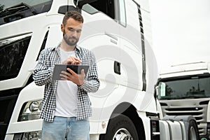 Young handsome truck driver is standing with a tablet near the truck